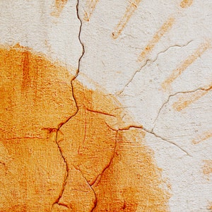May include: Close-up of a textured wall with a cracked surface. The wall has a white base with orange and brown paint splotches and streaks. Diagonal orange lines are visible on the upper right side of the image.