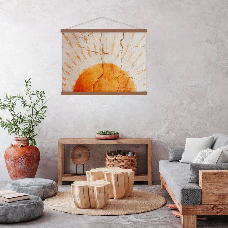 May include: A framed wall art print featuring an abstract design of a sunburst in shades of orange and cream. The artwork is displayed on a wooden frame and hangs in a modern living room setting.
