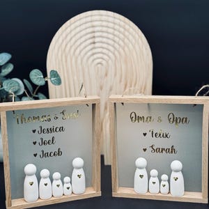 Könnte beinhalten: Zwei Holzrahmen mit grauen Hintergründen und weißen Holzfiguren. Der obere Rahmen sagt "Thomas & Susi" mit den Namen "Jessica", "Joel" und "Jacob" darunter. Der untere Rahmen sagt "Oma & Opa" mit den Namen "Felix" und "Sarah" darunter.