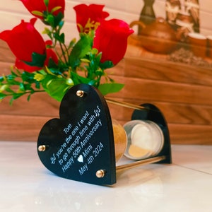 May include: A black heart-shaped hourglass with gold accents. The heart is engraved with the text "Tom If you're the one I want to go through time with S Happy 50th Anniversary Mimi May 4th 2024".
