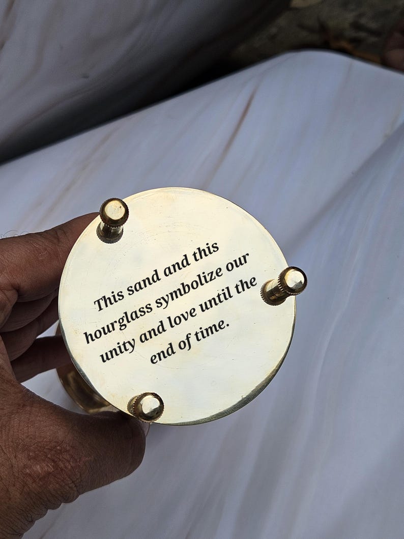 May include: A brass hourglass with a circular base and top. The top is engraved with the words "This sand and this hourglass symbolize our unity and love until the end of time."