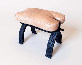 アンティークのラクダの鞍、素朴な木製の足置き、古びた素朴な布張りの