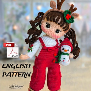Puede incluir: Patrón de crochet para una muñeca de Navidad con un atuendo rojo y blanco, cabello castaño y una diadema de reno. La muñeca sostiene un pequeño muñeco de nieve.