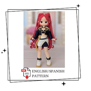 Puede incluir: Una muñeca de ganchillo con largo cabello rojo, que viste una chaqueta corta azul oscuro con ribetes dorados, una falda blanca y azul oscuro, y zapatillas blancas. La muñeca tiene piel clara y ojos oscuros. Incluye patrón PDF en inglés/español.