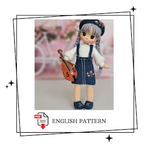 May include: A handmade crochet doll with a blue denim dress, white top, and a matching hat adorned with flowers. The doll holds a small orange violin. The text "ENGLISH PATTERN" is displayed below the doll.