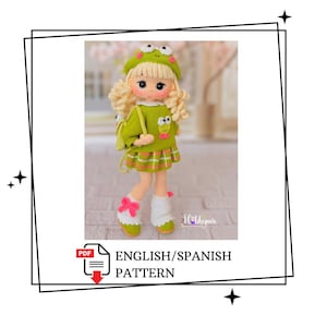 May include: A crocheted doll with blonde curly hair, wearing a green frog-themed beret, a green sweater with a frog face, a plaid skirt, white leg warmers with pink bows, and a small green backpack. The text reads ENGLISH/SPANISH PATTERN.
