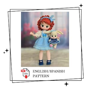 May include: A handmade crochet doll with red hair, a blue dress, and blue shoes, holding a small bunny doll. The bunny wears a blue and white striped dress. The image includes the text "ENGLISH/SPANISH PATTERN".
