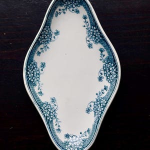 May include: White ceramic serving dish with a blue floral pattern. The dish has an elongated, diamond-like shape with a scalloped edge. The blue floral design is concentrated around the edges and along the center of the dish.