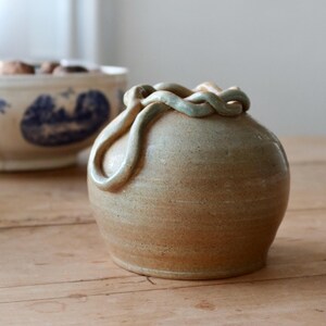 Peut inclure: Un vase en céramique brun clair avec un glaçage vert et un design unique en forme de corde autour du haut.