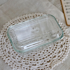 May include: A clear glass butter dish with a lid. The dish has a raised, circular design on the lid with the word "Fire King" embossed in the centre.