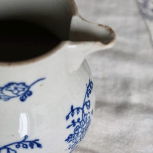 Puede incluir: Una jarra de cer&aacute;mica blanca con dise&ntilde;os florales azules. La jarra tiene un pico y un asa. El interior es oscuro. La jarra est&aacute; sobre una superficie de color claro.