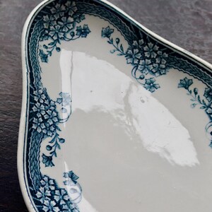 May include: White ceramic serving dish with a blue floral border. The dish has a unique, elongated shape and a glossy finish. The blue floral pattern includes detailed flowers and leaves, adding a touch of elegance to the tableware.