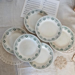 May include: Set of six white ceramic plates with a green and white geometric pattern around the rim.