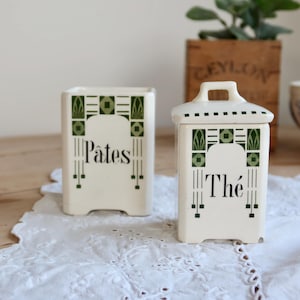 Op de afbeelding: Twee off-white keramische voorraadpotten met een vierkante basis en groene geometrische patronen. De ene pot is open en gelabeld met Pâtes in zwarte letters, de andere heeft een bijpassend deksel met handvat en het label Thé in zwart.