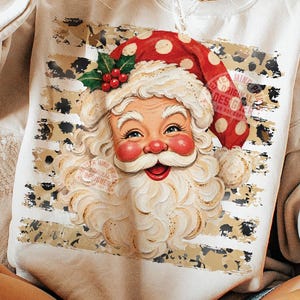 May include: A beige crewneck sweatshirt featuring a graphic of Santa Claus wearing a red hat with white polka dots and a sprig of holly. The design is set against a background of horizontal stripes with a black and tan leopard print pattern.