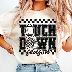 May include: A white t-shirt with a black graphic that says "Touch Down Season" with a football and a football helmet. The graphic has a checkered pattern.