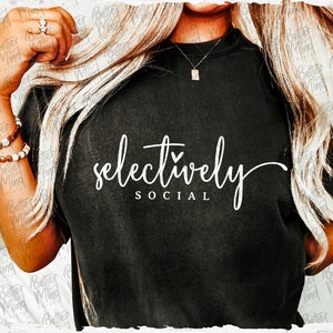 Puede incluir: Una camiseta negra con texto blanco que dice "selectively social" con un pequeño corazón sobre la palabra "selectively".
