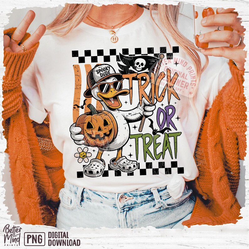 May include: White t-shirt with a Halloween-themed graphic. The design features a cartoon duck wearing sunglasses and a hat, holding a carved pumpkin and a flag that says "Trick or Treat". The duck is wearing Crocs. The shirt has the words "Spooky Dude".