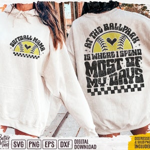 May include: Two white hoodies with a softball theme. One hoodie says "Softball Mama" with a yellow softball and black heart. The other hoodie says "At the Ballpark is where I spend most of my days" with a yellow softball and black heart.