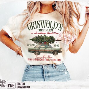May include: Cream-colored t-shirt featuring a graphic of a green car carrying a Christmas tree, with the text "Griswold's Tree Farm" and "Since 1989". The shirt also includes the phrase "home for the fun old fashioned family Christmas".