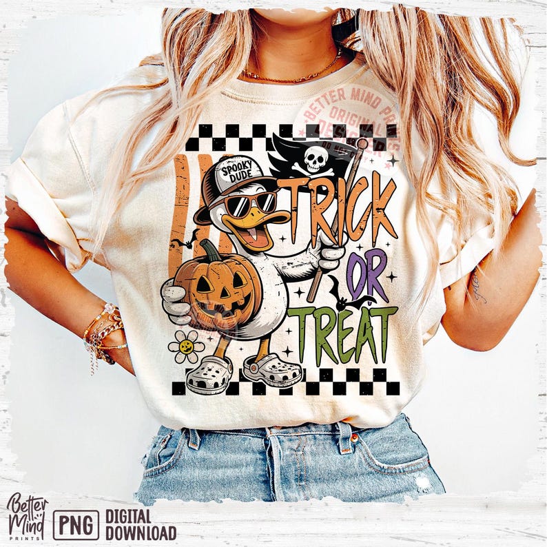 May include: Cream-colored t-shirt featuring a cartoon duck wearing sunglasses and a hat, holding a jack-o'-lantern and a flag that says "Trick or Treat." The duck is wearing Crocs. The shirt has a Halloween theme.