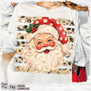 May include: A light gray heathered sweatshirt featuring a graphic of Santa Claus with a white beard, red cheeks, and a red hat with white polka dots. The design includes a background of horizontal stripes with a black and tan leopard print pattern.