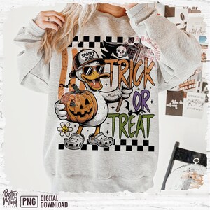 May include: A gray sweatshirt with a Halloween-themed graphic. The graphic features a cartoon duck wearing sunglasses and a hat, holding a pumpkin and a trick-or-treat sign. The words "Trick or Treat" are prominently displayed.