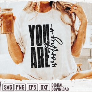 May include: White t-shirt with the text "YOU ARE worthy" in black. The shirt is a digital download. A glass jar with a wooden lid is held in the left hand.