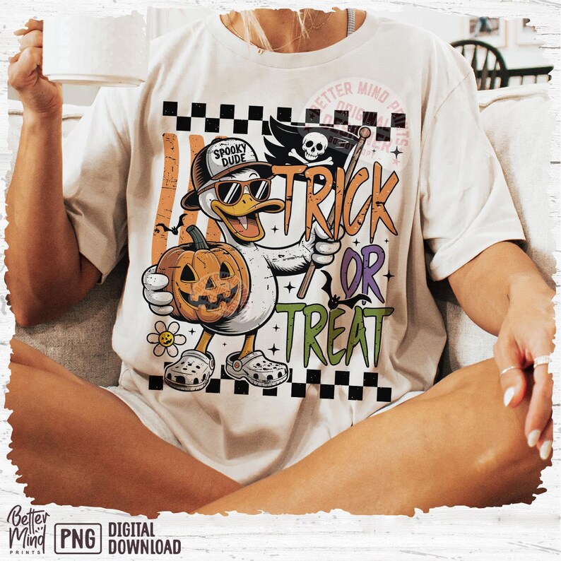 May include: Cream-colored t-shirt featuring a cartoon duck wearing sunglasses and a hat that says "Spooky Dude." The duck holds a carved pumpkin and a flag that says "Trick or Treat." The shirt has a Halloween theme.