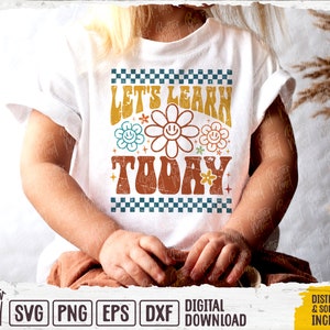 May include: A white t-shirt with a retro-style design featuring the text "Let's Learn Today" in a colorful, distressed font. The design includes a checkered pattern and stylized flowers with smiley faces.