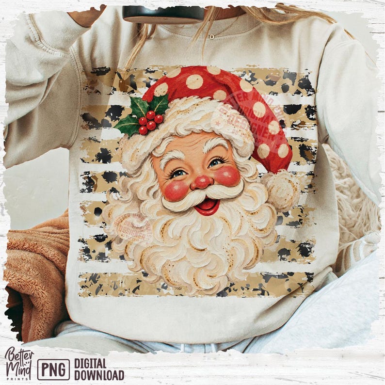May include: A beige long-sleeve sweatshirt featuring a graphic of Santa Claus with a white beard, red cheeks, and a red polka-dot hat with holly. The design is set against a background of horizontal stripes with a black and tan leopard print pattern.