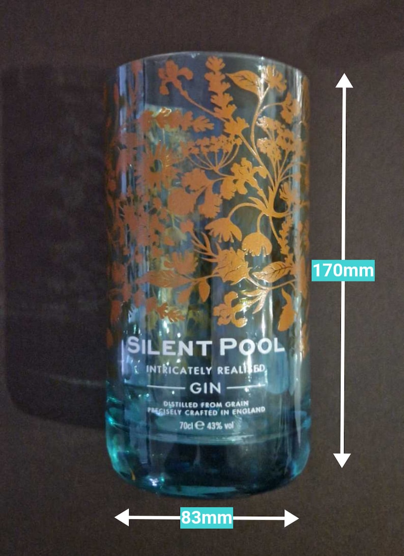 K&ouml;nnte beinhalten: Ein klares Glas, 170 mm hoch und 83 mm breit, mit t&uuml;rkisfarbenem Boden und goldenem Blumendesign. Der Text "SILENT POOL GIN" ist sichtbar. Der Gin wird aus Getreide destilliert und pr&auml;zise in England hergestellt.