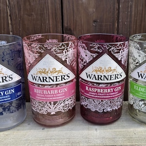 May include: Four glass bottles with different colored labels and Warner's Gin printed on them. The labels are for London Dry Gin, Rhubarb Gin, Raspberry Gin, and Elderflower Gin.