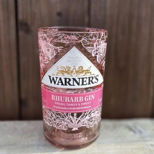 May include: A pink glass bottle of Warner's Rhubarb Gin. The label says "Farm Grown British Gins" and "Rhubarb Gin Fresh, Tangy & Sweet". 1/3 of this bottle is pure rhubarb juice.