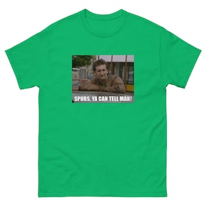 May include: A vibrant green t-shirt with a rectangular graphic. The graphic shows a man and the text "SPURS, YA CAN TELL MAN!" in white. The t-shirt is a short-sleeved, crew neck style.