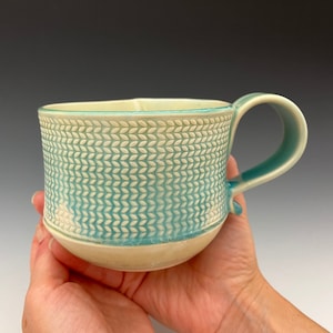 May include: A ceramic mug with a light blue and white patterned design. The mug has a rounded shape and a handle.