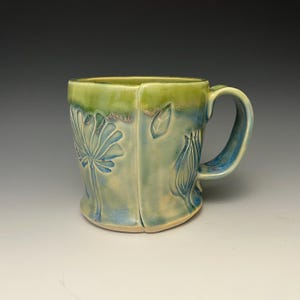 May include: A ceramic mug with a green and blue glaze. The mug has a floral design embossed on the side.