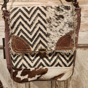 May include: A brown and white patchwork crossbody bag with a chevron pattern and a flap closure. The bag has a brown leather strap and a brown leather trim.