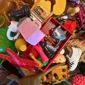 May include: A collection of small toys and figurines in various colors. Includes a pink pitcher, a red tray with chess pieces, a miniature dinosaur, a checkerboard shoe, and a miniature washboard with the text "Little Daisy".