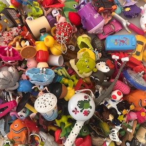 May include: A large collection of assorted miniature plastic toys including a Shrek figure, a Hello Kitty character, a FleetPride football, a white frog rattle, a Nemo fish, a yellow rubber duck, and various small vehicles and dolls.