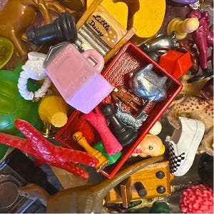 May include: A collection of small, colorful toys and figurines. Includes a pink pitcher, a red tray with various items, a miniature shoe with a checkered pattern, and a small dinosaur figurine. Other items include a miniature washboard with the text "Little Daisy".