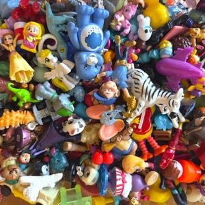 May include: A colorful assortment of small plastic toys, including figurines, vehicles, and animals. The toys are in various colors, such as red, blue, yellow, and purple. The collection includes a zebra, a dinosaur, and a Care Bear.