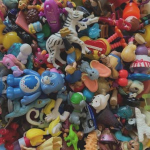 May include: A colorful assortment of children's toys, including figurines, animals, and cartoon characters. The toys are in various colors and sizes, with a zebra figurine prominently displayed. Other toys include a blue Care Bear and a green dinosaur.