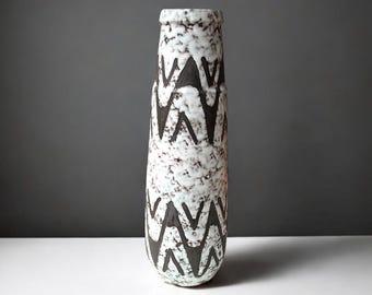 May include: A white ceramic vase with a black geometric pattern. The vase has a textured surface and a rounded shape.
