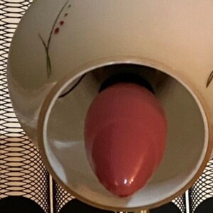 May include: A white ceramic lampshade with a floral design and a pink light bulb inside.