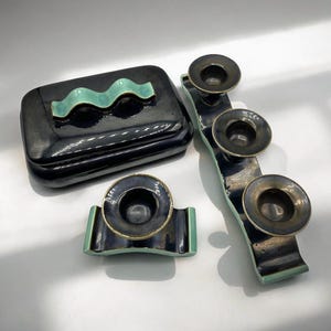 May include: A set of three black and green ceramic candle holders with a wavy design. The holders are in the shape of a long, narrow rectangle with three round candle cups.