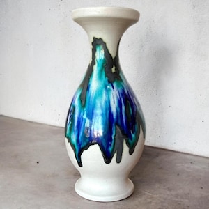 Könnte beinhalten: Eine weiße Keramikvase mit einem abstrakten Design in Blau, Grün und Schwarz. Die Vase hat eine breite Öffnung und einen schmalen Boden.