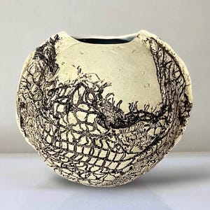 May include: A white ceramic vase with a black and white design. The vase has a round shape and a wide opening.
