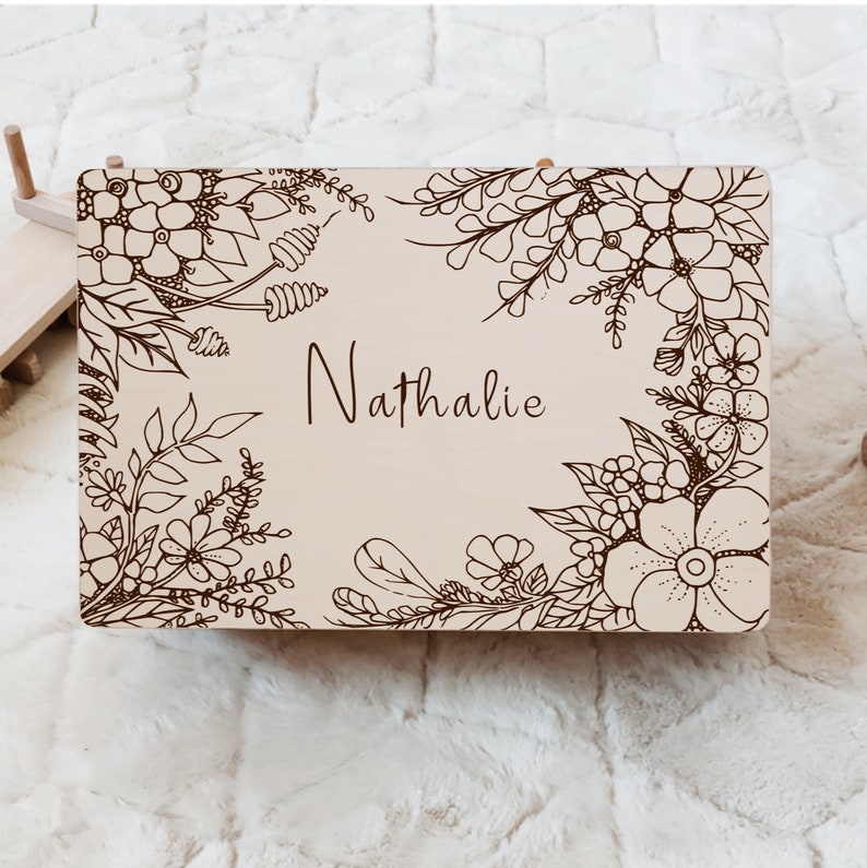 May include: A light brown wooden box with a floral design engraved on the front. The name "Nathalie" is engraved in the center of the box.