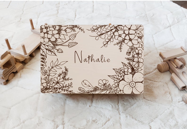 May include: A wooden sign with a floral design and the name "Nathalie" engraved in the center. The sign is light brown and has a natural wood finish.
